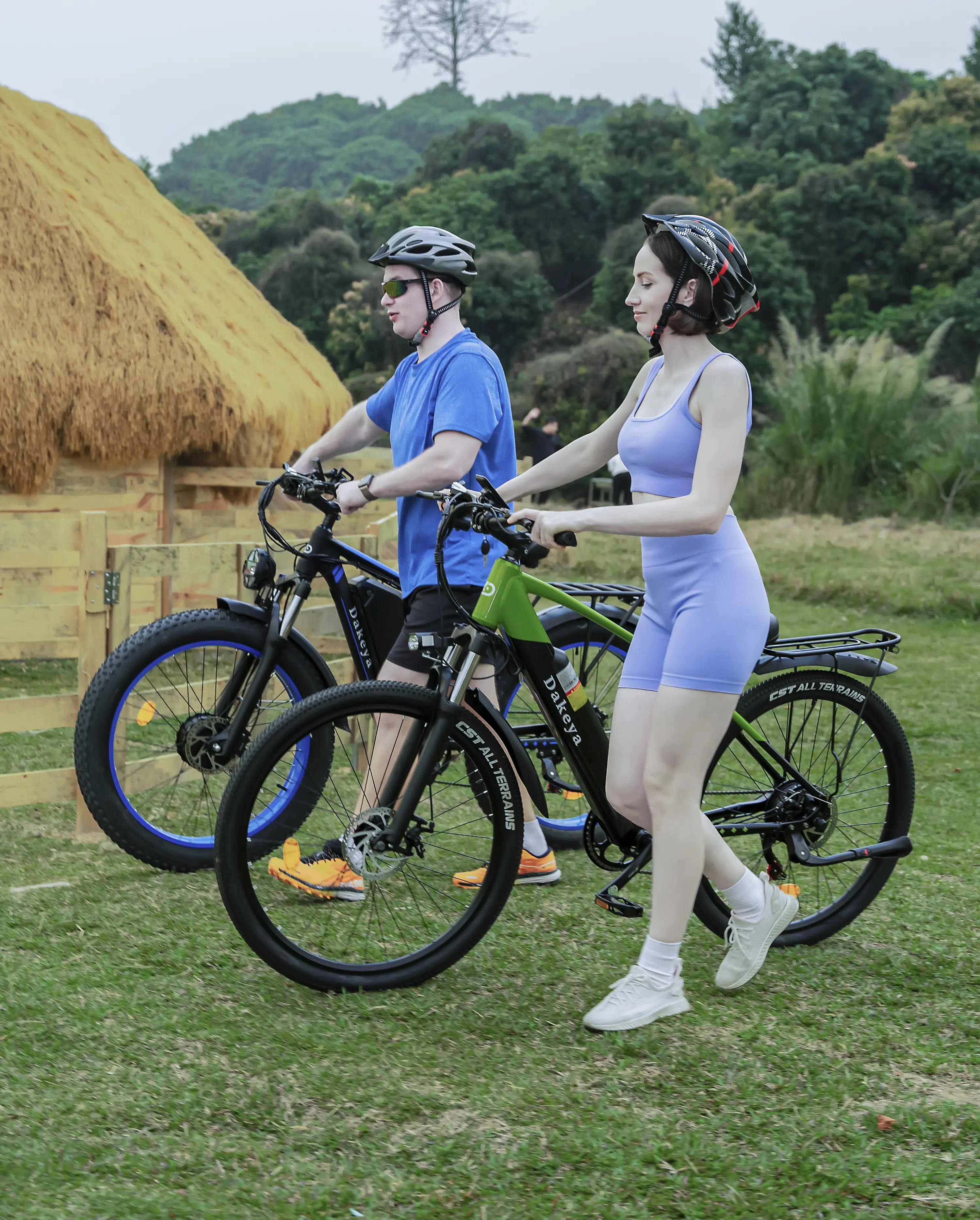Man and woman walking Dakeya fat tire electric bikes on grassy outdoor trail